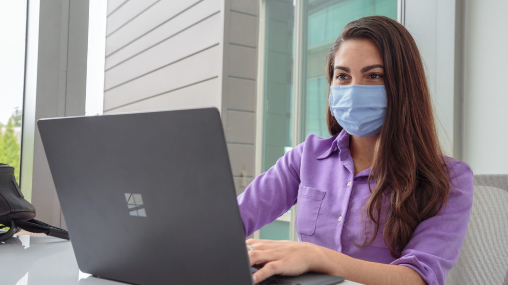 A young woman wearing a mask and working on a computer
