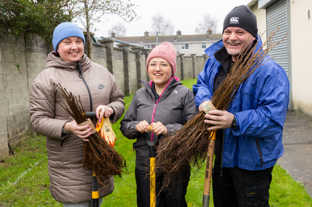 Three people holding tree saplings