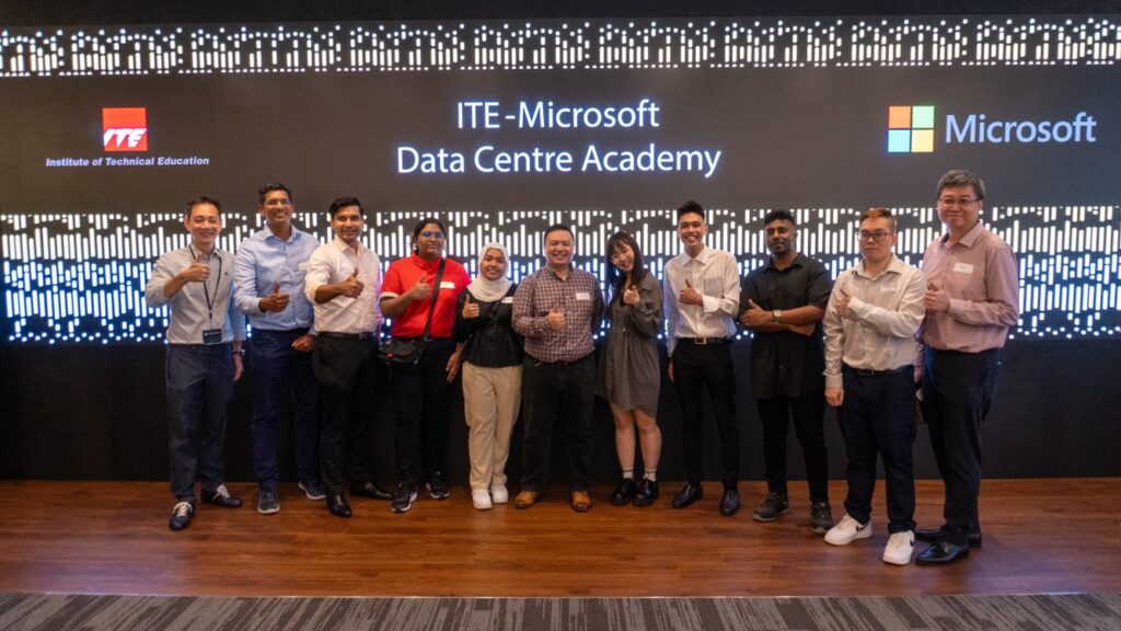 A group of people standing and smiling in front of a sign showing ITE_Microsoft Data Centre Academy