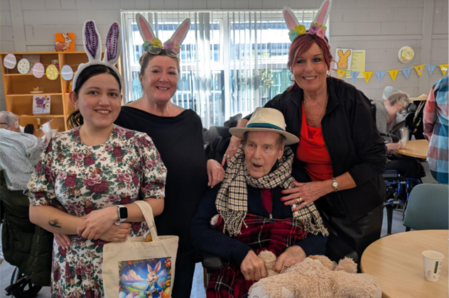 Three people wearing Easter bunny ears standing around an elderly person in a wheelchair